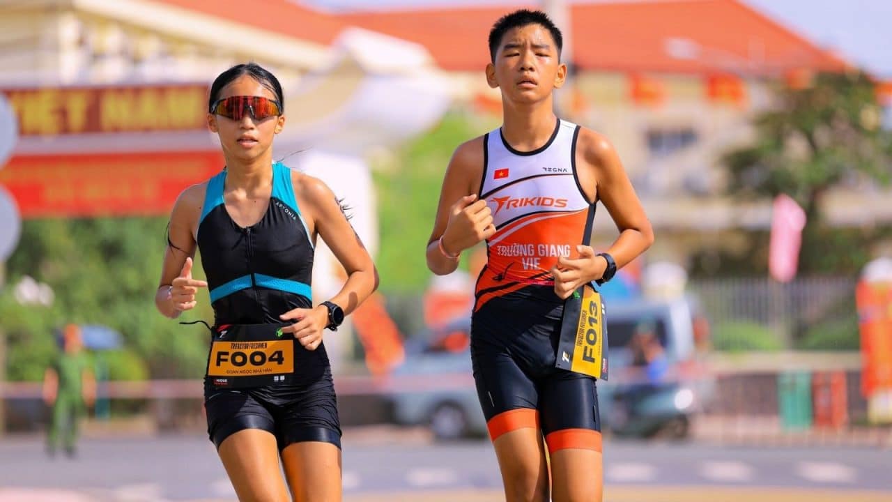 Hai vận động viên trẻ Nhã Hân và Trường Giang đang chạy trên đường đua Triathlon trong trang phục TriKids